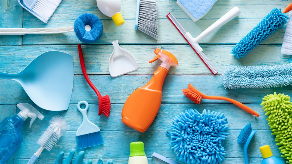 Colorful cleaning brushes, sponges, cloths and spray bottles laid out on a blue wooden surface