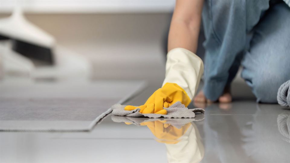A gloved hand wiping a tiled floor by hand