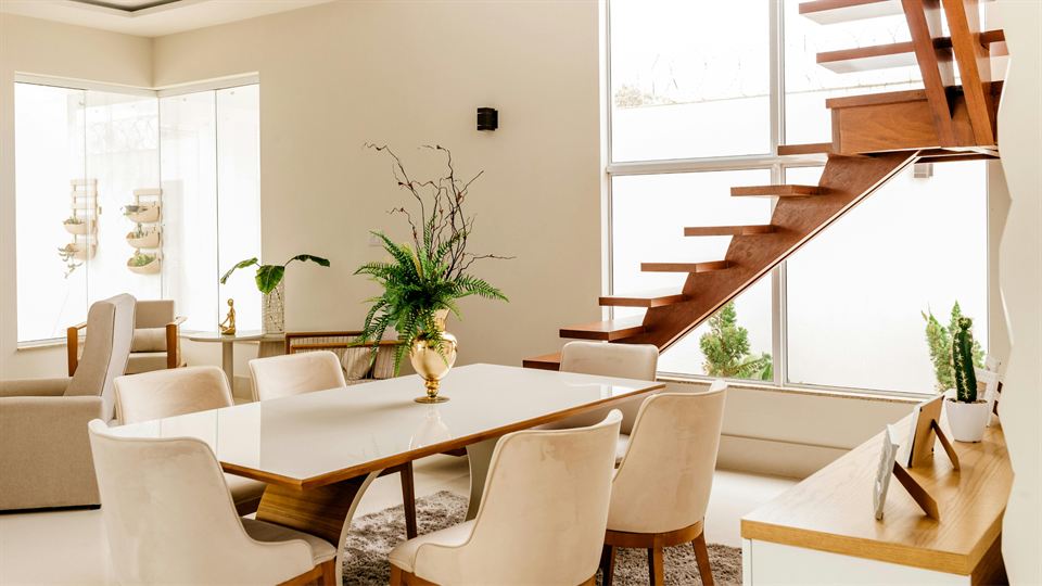 A bright, tidy dining room with a wooden staircase and large windows