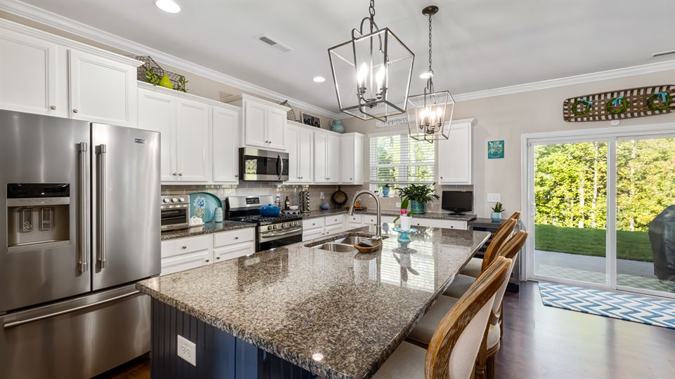 A bright, clean kitchen with a granite island, white cabinets and pendant lights