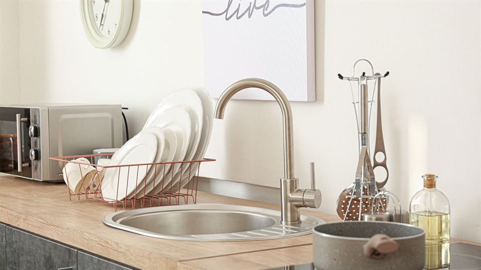 A tidy kitchen sink and counter with clean dishes drying in a rack
