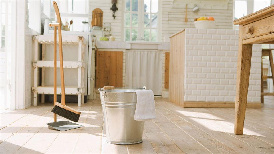 A broom, dustpan and bucket in a sunlit kitchen